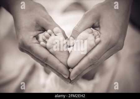 Les pieds de bébé nouveau-né dans les mains de sa mère en forme de coeur. Mère montrant son amour et son affection. Monochrome Banque D'Images