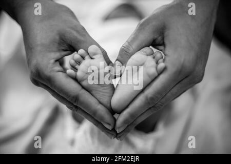 Les pieds de bébé nouveau-né dans les mains de sa mère en forme de coeur. Mère montrant son amour et son affection. Noir et blanc Banque D'Images