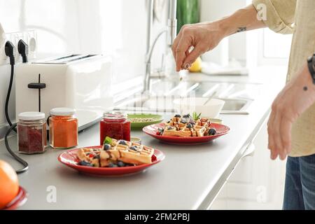 Des noix éparses à la main pour hommes sur des gaufres cuites pour préparer le petit déjeuner à la maison. Banque D'Images