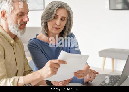 Un couple plus âgé vérifie des documents bancaires ou des factures à l'aide d'un ordinateur portable à la maison. Banque D'Images