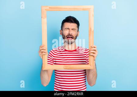 Photo d'un jeune homme triste maltraité habillé t-shirt tenue cadre marron pleurs isolé arrière-plan bleu Banque D'Images
