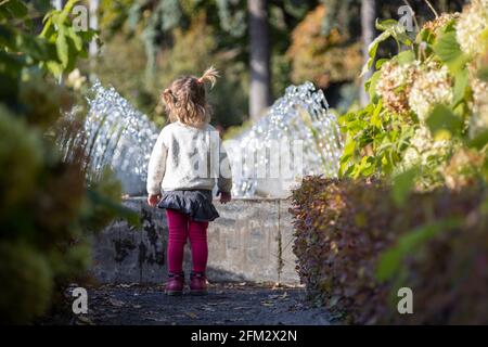 une adorable petite fille regarde la fontaine. elle est petite dans un parc avec des fontaines par temps ensoleillé. week-end en famille. petite fille qui regarde dans une fontaine Banque D'Images