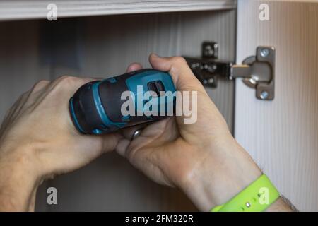 Un homme méconnaissable installe une porte sur une armoire, fixe les meubles à l'aide d'un tournevis. Seules les mains sont visibles. Gros plan. Concept de rénovation, mobilier Banque D'Images