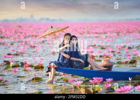 Deux belles femmes naviguant sur un lac avec des fleurs de lotus rose, Thaïlande Banque D'Images