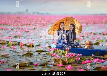 Deux belles femmes naviguant sur un lac avec des fleurs de lotus rose, Thaïlande Banque D'Images