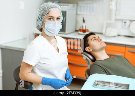 Une femme dentiste se tient dans le cabinet dentaire. Patient heureux en arrière-plan. Concept de soins et de santé dentaires. Banque D'Images