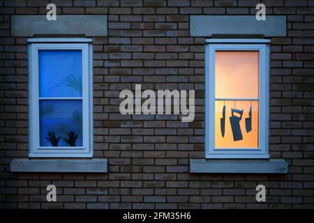 Deux silhouettes de fenêtre sur le thème de la maison hantée d'Halloween : couteaux et une scie accrochée dans une fenêtre éclairée ; mains essayant de s'échapper d'une autre. Banque D'Images