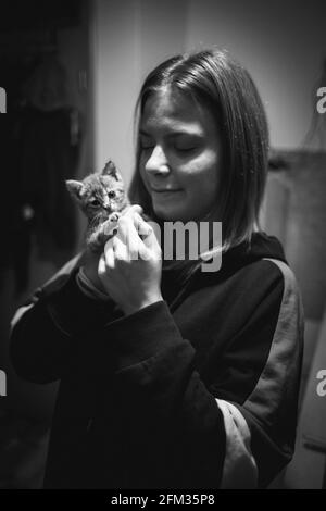 Prise de vue verticale en niveaux de gris d'une jeune femme caucasienne posant avec son joli petit chaton Banque D'Images