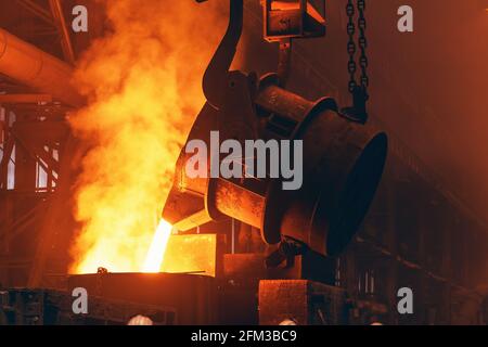 Le métal fondu s'écoule du grand récipient dans le moule à sable avec des étincelles. Coulée de fer dans une usine de fonderie métallurgique, industrie lourde. Banque D'Images