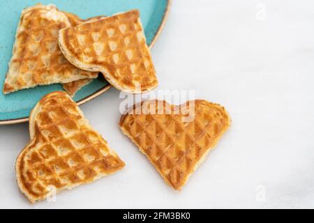 Gaufres en forme de cœur éparpillées dans une assiette verte sur du blanc table en marbre Banque D'Images