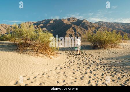 Death Valley, Californie, États-Unis - 14 avril 2021. Femme mature avec bouteille d'eau et randonnée pédestre en canne dans le désert. Dunes de sable de Mesquite dans Death va Banque D'Images