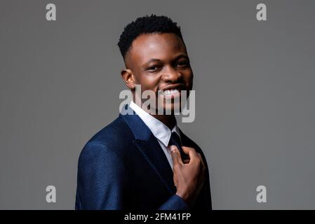 Jeune homme africain souriant et joyeux portant un costume d'affaires formel en studio, fond gris isolé Banque D'Images