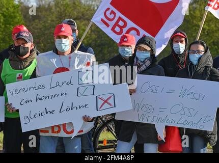 06 mai 2021, Brandebourg, Beeskow: Les employés du fabricant d'emballages Linpac ont deux panneaux indiquant "united Country, One group, same Wages" et "Ossi = Wessi, Wessi = Ossi, we are one country!" lors d'une grève d'avertissement devant les locaux de l'usine. Jeudi matin, les employés du fabricant d'emballages Linpac à Beeskow (district d'Oder-Spree) ont cessé de travailler. La grève d'avertissement de 24 heures a été déclenchée par l'Union industrielle des mines, de la chimie et de l'énergie (IG BCE). Avec l'action industrielle, le syndicat veut réaliser un contrat de maison propre pour l'entreprise. Employés de Linpac dans Bees Banque D'Images