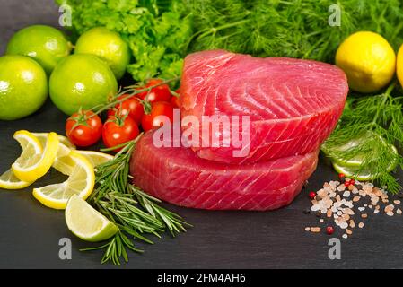 Thon cru Steak, thon sashimi, thon poisson tranché avec des légumes. Manger sainement avec des fruits de mer, nous cuisons à la maison. Disposition de la viande de poisson sur pierre noire Banque D'Images