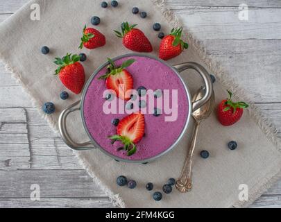 yaourt fraîchement préparé avec myrtilles et fraises servi dans un bol sur fond beige en bois Banque D'Images