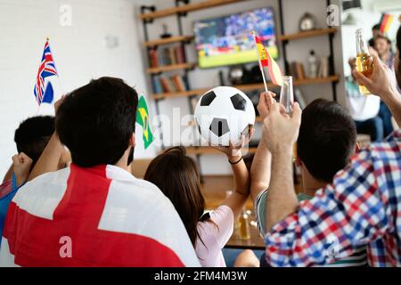 Divers amis fans de sport regardant un match de football à la télévision à la maison. Célébration de la crier excitée Banque D'Images