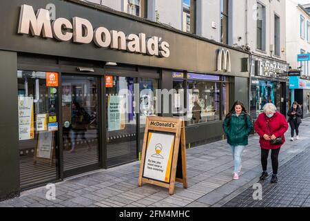 Les gens marchent après un panneau qui dit "par la loi, vous devez porter un couvre-visage" à l'extérieur de McDonalds, Cork, Irlande. Banque D'Images
