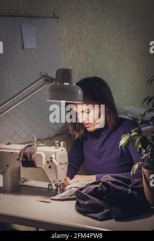 Femme couturière coudre des vêtements - veste tendance en velours sur une machine à coudre dans son studio. Banque D'Images