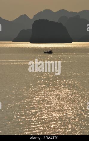 Vue panoramique du coucher de soleil sur les eaux étincelantes, les formations rocheuses, les montagnes bleues et les bateaux flottants sur la baie de Halong au Vietnam Banque D'Images