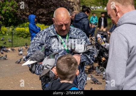 LONDRES, Royaume-Uni – 1er mai 2021 : un vieillard excentrique est vu avec des pigeons perchés sur ses bras pendant qu'il nourrit les oiseaux dans un parc local. Banque D'Images