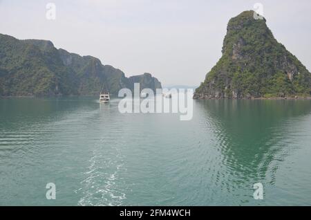 Vue panoramique du coucher de soleil sur les eaux étincelantes, les formations rocheuses, les montagnes bleues et les bateaux flottants sur la baie de Halong au Vietnam Banque D'Images