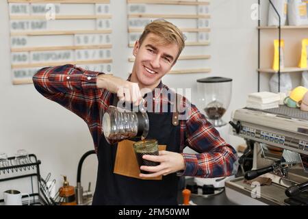 le barista en tablier verse du café frais dans une tasse Banque D'Images