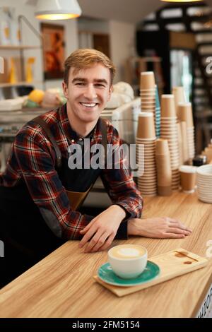 bon serveur dans un tablier tenant une tasse de boisson chaude Banque D'Images