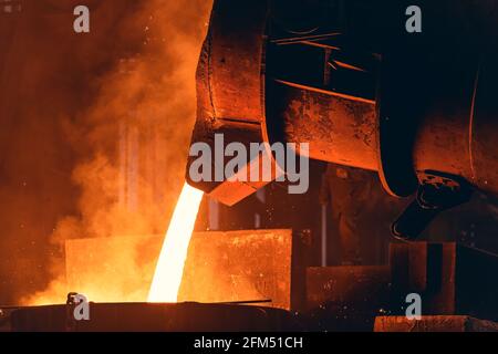 Le métal fondu s'écoule du grand récipient dans le moule à sable. Coulée de fer dans une usine de fonderie métallurgique, industrie lourde. Banque D'Images
