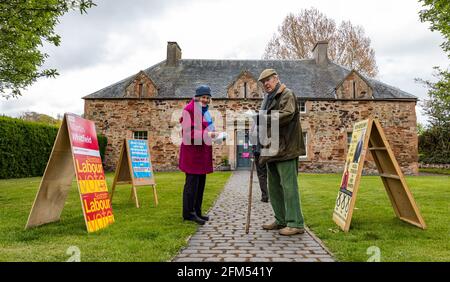 East Lothian, Écosse, Royaume-Uni, 6 mai 2021. Élections écossaises : l'un des bureaux de vote du comté alors que le peuple écossais va aux urnes. Photo : un couple âgé se prépare à voter à l'ancienne salle pittoresque du village de Tyninghame, qui est transformée en un lieu de vote avec des bureaux de vote des partis politiques électoraux locaux à l'extérieur Banque D'Images