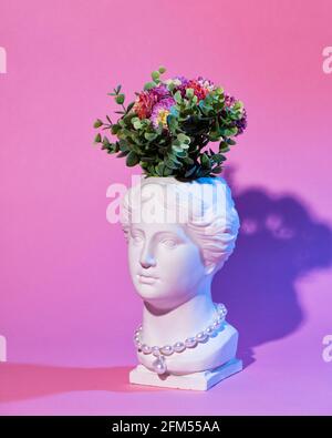 Jardinière à tête en plâtre de Vénus tendance avec perles et bijoux en or sur fond rose et bleu. Copie de gypse fait face à une ancienne statue ou sculpture avec une gree Banque D'Images