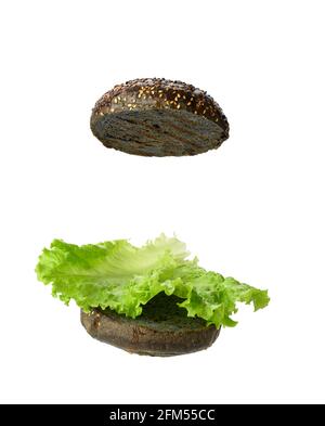 la feuille de laitue verte repose sur la moitié d'un petit pain rond noir, la nourriture est isolée sur un fond blanc Banque D'Images