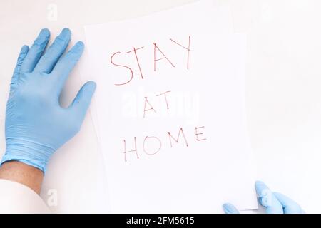 main du médecin dans des gants en latex tenant un papier écrit séjour à la maison . Banque D'Images