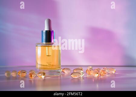 Huile pour le visage jaune en bouteille de verre avec capsules de beauté sur fond rose clair et bleu avec ombres géométriques. Vue avant Banque D'Images