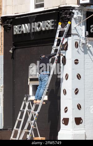 Un peintre peint un panneau pour une nouvelle entreprise s'ouvrant sur la 29e avenue à Flushing, Queens, New York. Banque D'Images