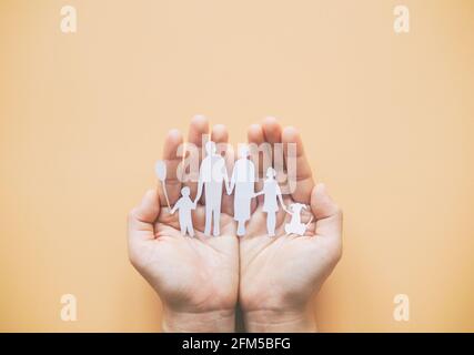 Main tenant le papier de famille coupé sur fond jaune. Concept de la Journée de la famille, soins d'accueil, violence familiale, école familiale, journée internationale des familles, wor Banque D'Images