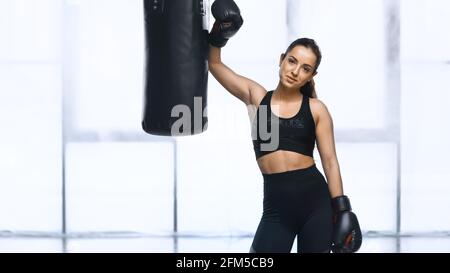 épuisé sportswoman en gants de boxe et vêtements de sport debout près de la perforation sac dans la salle de sport Banque D'Images