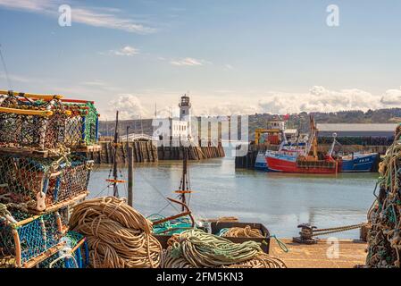 Les bateaux de pêche sont amarrés le long d'un quai et un phare est d'un côté. Une passerelle relie les jetées. Pots et cordes de homard. Banque D'Images