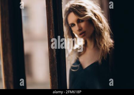 Portrait artistique défoqué d'une belle femme blonde aux yeux fumés avec maquillage à travers le verre en teinte beige. Banque D'Images