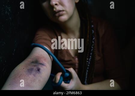 Fille adulte avec des dreadlocks avant de prendre la dose de stupéfiant dans la veine. La femme drogué tire sa main avec le tourniquet. Ponction des plaies et des ecchymoses sur le bras de la femme. Banque D'Images