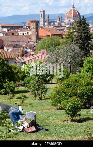 Lecture d'un livre, allongé sur la pelouse, au Giardino delle Rose (près de la Piazzale Michelangelo), lors d'une chaude journée de printemps. Vue imprenable sur la ville. Banque D'Images