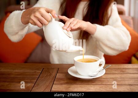 une fille boit du thé de désintoxication à base de plantes dans un café. Table de tasse blanche dans le café. Femme buvant du thé sur une table en bois Banque D'Images