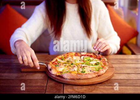 Cueillette à la main d'une tranche de pizza maison à l'aide d'un coupe-pizza. Manger de la pizza à la maison Banque D'Images