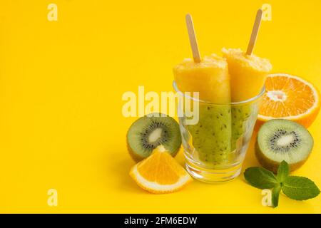 Des popsicles avec kiwi et fruit orange sur fond jaune. Copier l'espace. Banque D'Images