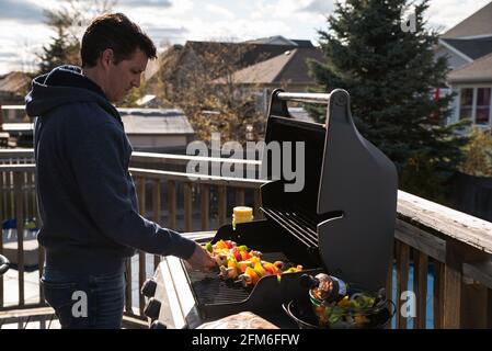 Homme mettant des brochettes de légumes sur un barbecue à gaz à l'extérieur. Banque D'Images