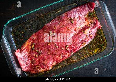 Steak de bœuf mariné dans un plat de verre : un steak de flanc cru marinant dans un plat de cuisson en verre Banque D'Images