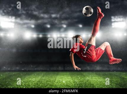 Un joueur de football en uniforme rouge frappe le ballon avec un un coup acrobatique dans les airs au stade Banque D'Images