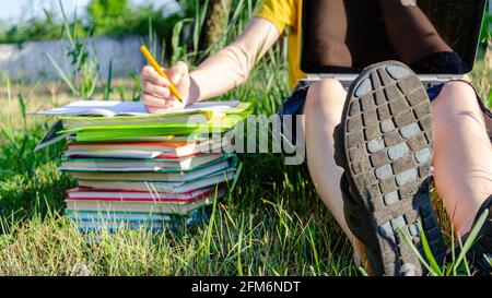 Le gars est un étudiant, un écolier est engagé, fait des devoirs avec un ordinateur portable en ligne dans le jardin sous l'arbre. Banque D'Images