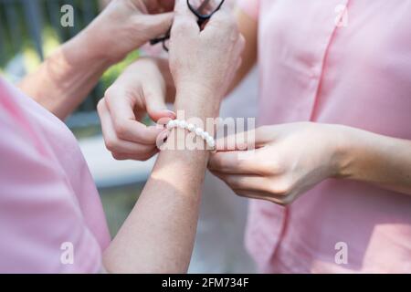 une femme fixe un bracelet de perle au poignet d'une autre femme vêtue de chemises roses ou de pyjamas Banque D'Images