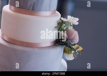 Gros plan d'un mariage gris et blanc à trois niveaux gâteau avec fleurs et ruban rose à un angle Banque D'Images