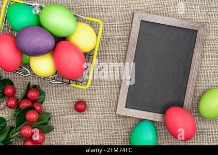 Oeufs de Pâques multicolores dans un panier en métal et un cadre avec un tableau de craie. Banque D'Images